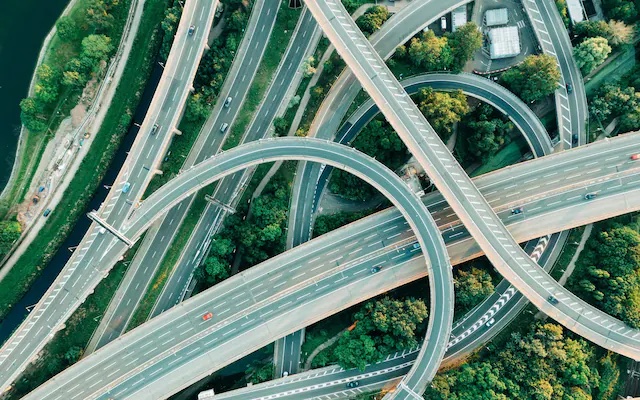 Aerial view of a tangled motorway interchange, flyovers looping over and under each other through green trees
