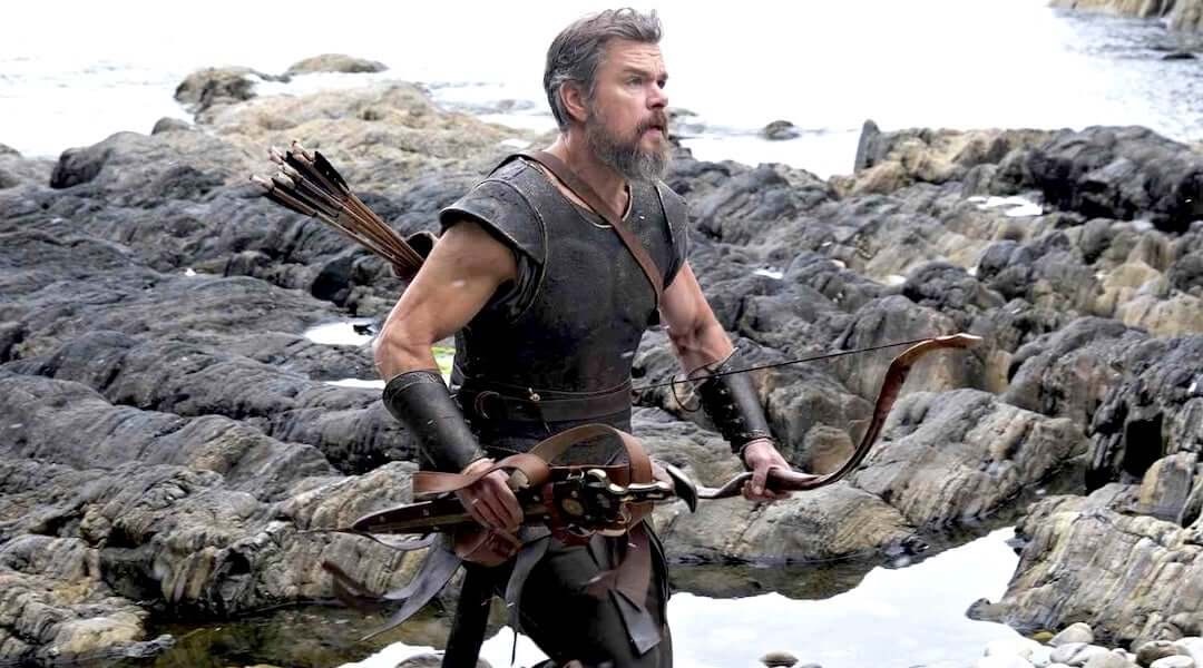 Matt Damon as Odysseus, well-fed and muscular, holding a bow on the rocks